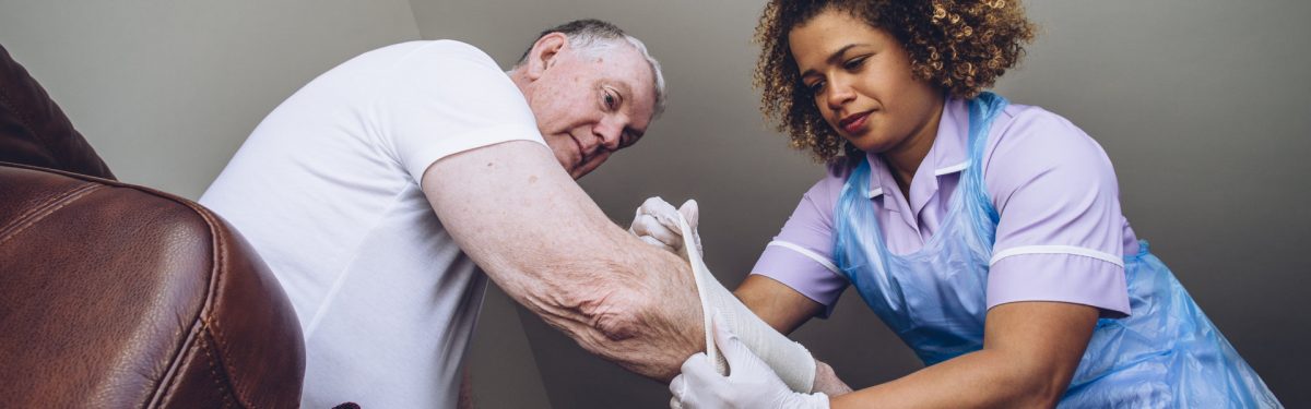 Caregiving Nurse putting a bandage on a senior mans arm in his home.